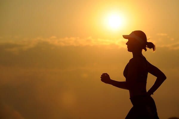 Silhouette of woman running over a backdrop of a setting sun.